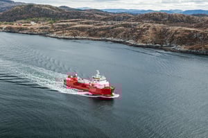 The image shows a red supply vessel cruising along a shoreline. The seas are calm. 