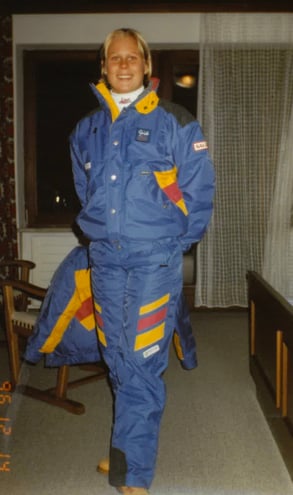 A picture of Anna Aulie, Marketing & Communications Manager at Hatteland Technology, from when she was a ski guide in Austria in the 1990s. She is wearing a blue ski suit from top to toe, with red and yellow markings. She is in a hotel room, smiling and facing the camera.