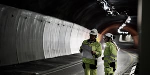Jan Olav Larsen and Mia Skrataas on a site visit to a road tunnel rehabilitation project, assessing the placement of CCTV cameras for complete AID coverage and -detection. In the background, an illuminated road tunnel.