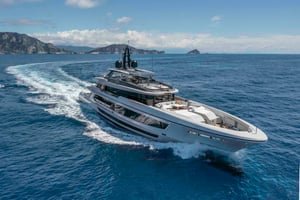 Superyacht Baglietto T52 is cruising on the open sea, with Mediterranean hills in the background. It's a sunny day, and calm waters.