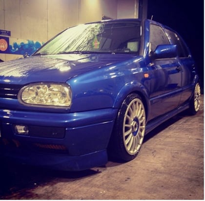 This radiant blue VW Golf is Gry Amalie Rosberg's first car. It has big rims and is lowered almost to the ground. The car is parked at a carwash.