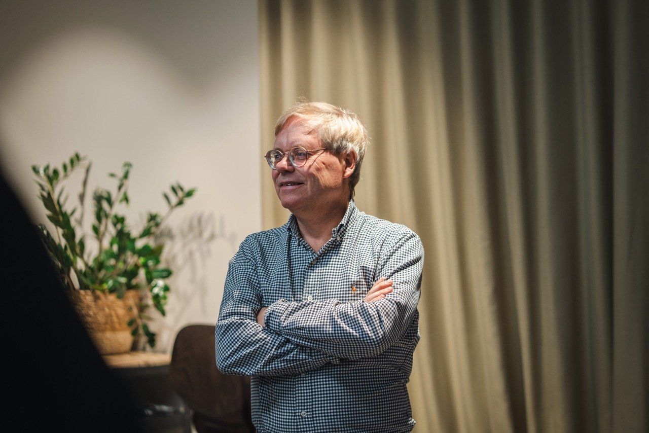 The picture shows Axis CEO and co-founder Martin Gren at Spoor's HQ in Oslo, Norway. He is smiling. He is wearing a checkered shirt. In the background is a beige curtain and a green succulent. 
