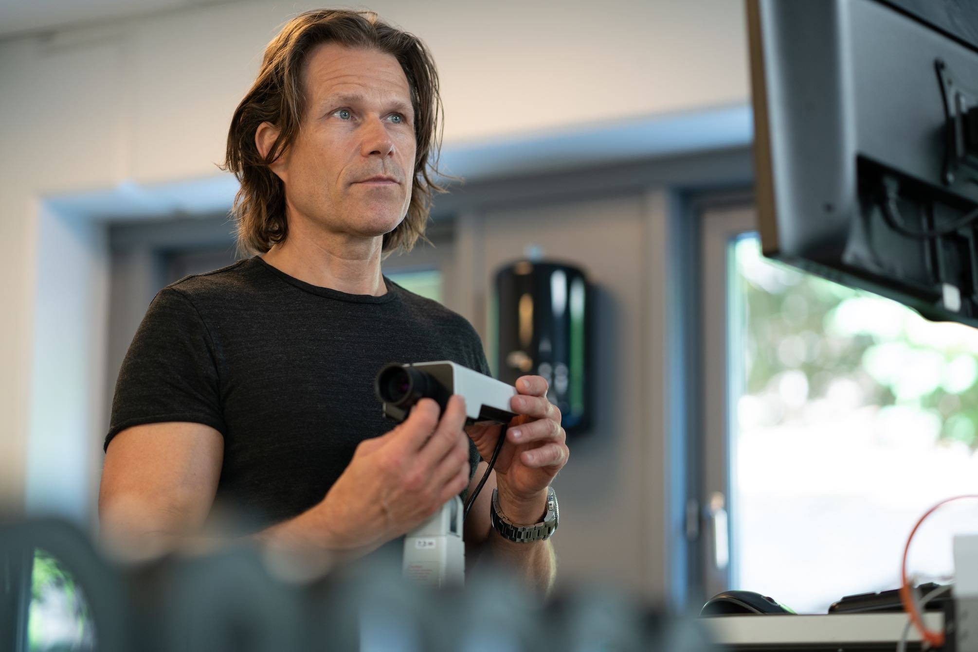 Kai Fossgård from Hatteland Technology is checking or preparing a CCTV camera for a tunnel. He is holding the camera, and is wearing a black t-shirt.