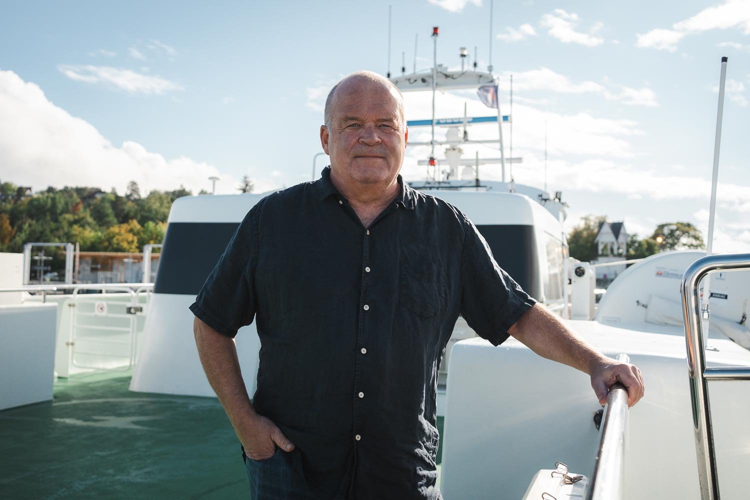 Marine CCTV expert Anders Bjerketveit is standing on the deck of a passenger ferry, with one hand on the rail. He is wearing a black, buttoned t-short. The weather is nice and the sea is calm. The pilothouse and the radar antenna is visible in the background.