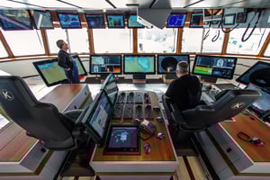 Two fishermen inspecting an array of maritime monitors on a ship bridge. The monitors are of various sizes, and. are produced by Hatteland Technology.