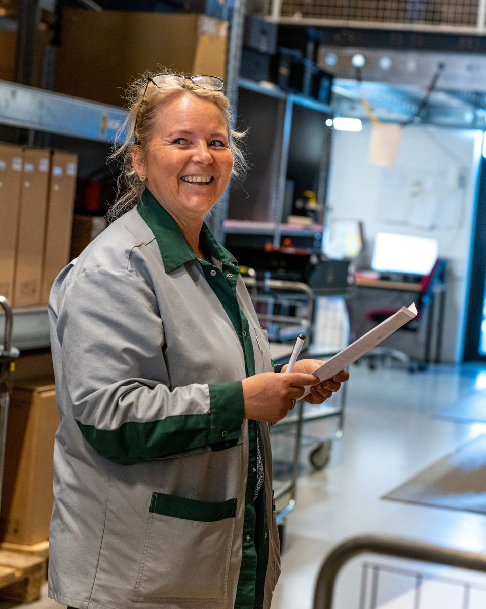 The picture shows a Hatteland Technology employee. She is turned sideways, holding a stack of papers and a pen. She is smiling.