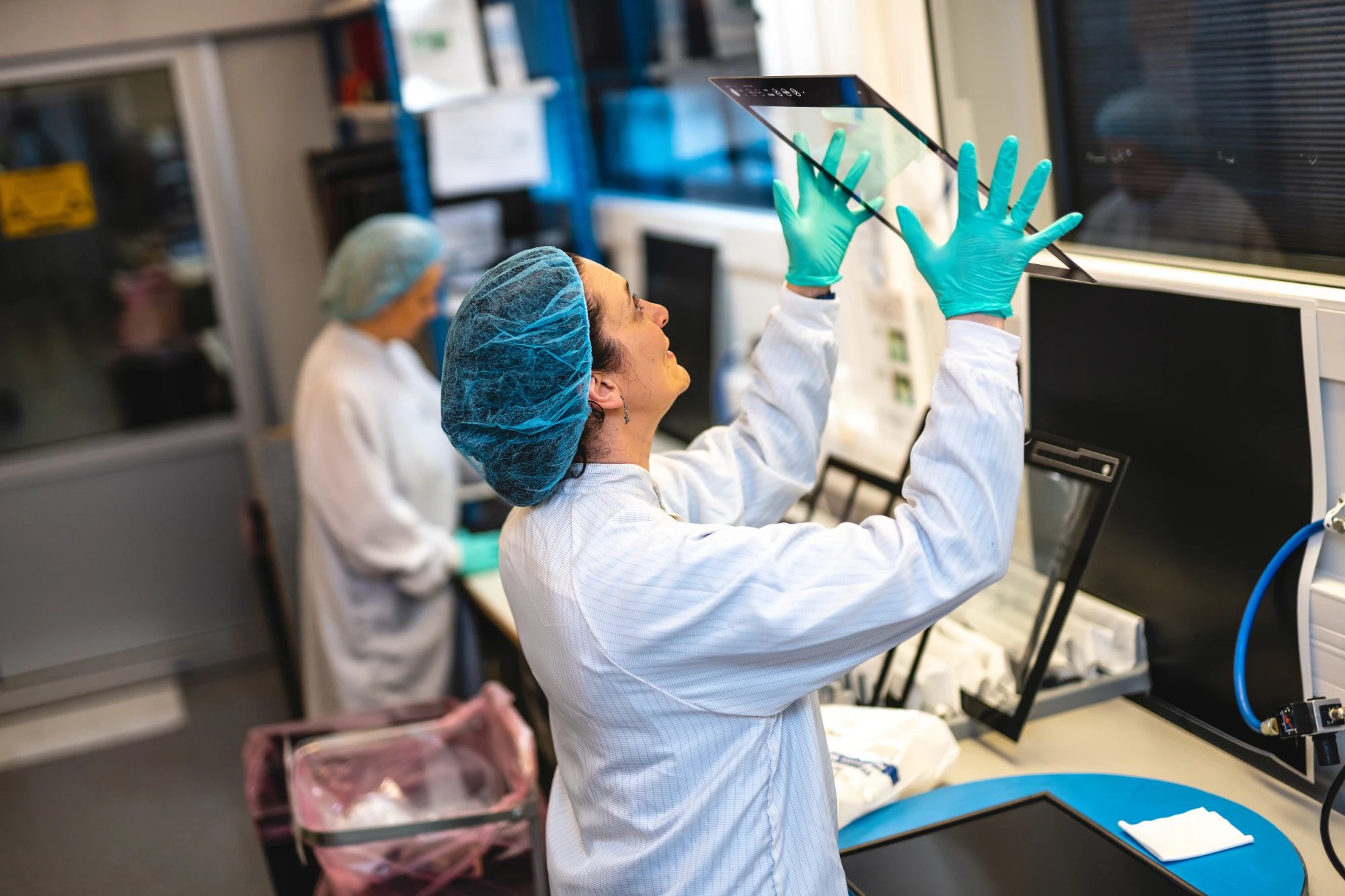 This image depicts a worker in the cleanroom in Aksdal, Norway. She checks a monitor glass for impurities. 