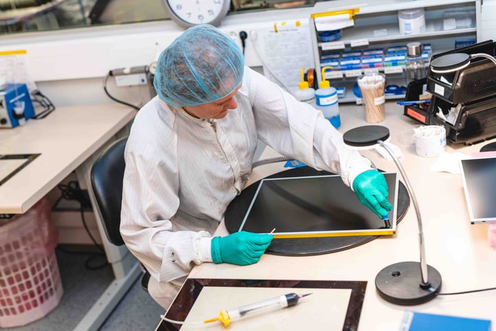 A worker is in midst of optically bonding a screen for a Hatteland Technology monitor. She is wearing protective gear to keep the unit free from impurities.  