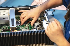 The image shows a worker assembling a Hatteland Technology computer at the manufacturing plant in Aksdal, Norway. The cabinet is open, showing the motherboard and internal electronics.
