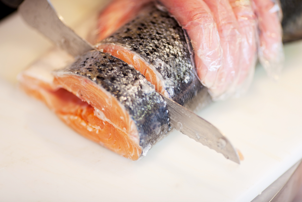 Closeup of female workers hands cutting fish on chopping board