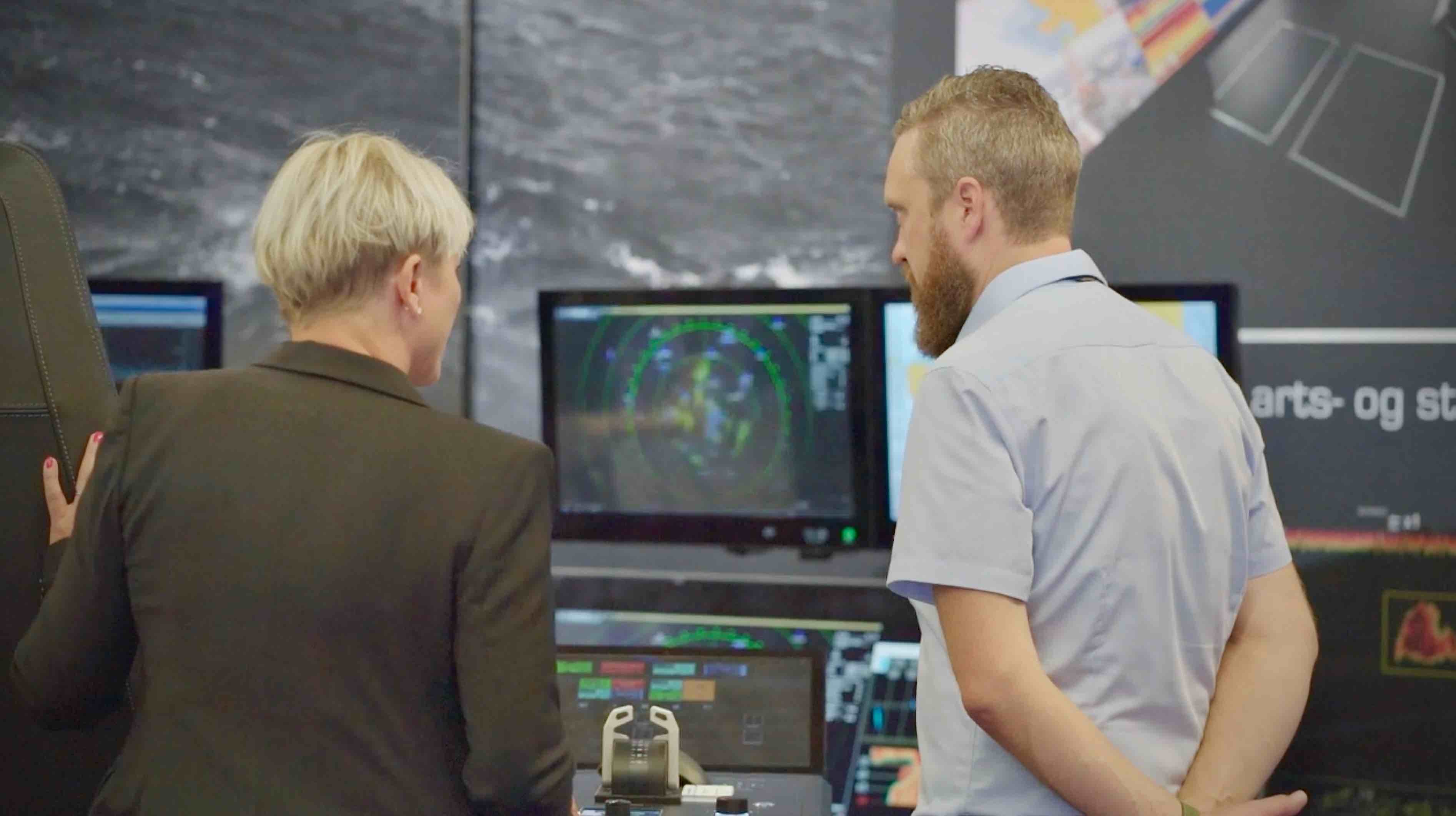 The picture shows part of the Furuno Norway stand, Nor-Fishing 2022 in Trondheim. Torhild Skrunes is in the left of the picture, discussing something with the Furuno Norway representative. There are maritime monitors in the background. 