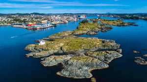 Aerial view of Haugesund, Norway, close to where Hatteland Technology's head quarters are situated. The image shows the coastline with several ships on the water, as well as houses and mountains in the background. It is a sunny day with calm waters.