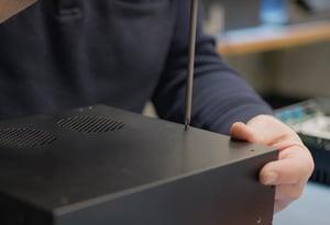This thumbnail shows a worker assembling an industrial computer at Hatteland Technology's Swedish office. The computer is black. The worker is using a screw driver.