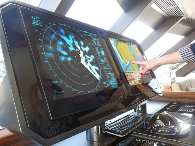 The picture shows the bridge on a boat, with two monitors visible. The closest one is a radar plotter, to its right is an electronic nautical chart.