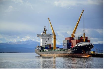 A cargo ship is unloading at the dock, with two yellow cranes. Digital loading systems are vulnerable to cyber attacks while interfacing with shore systems. 