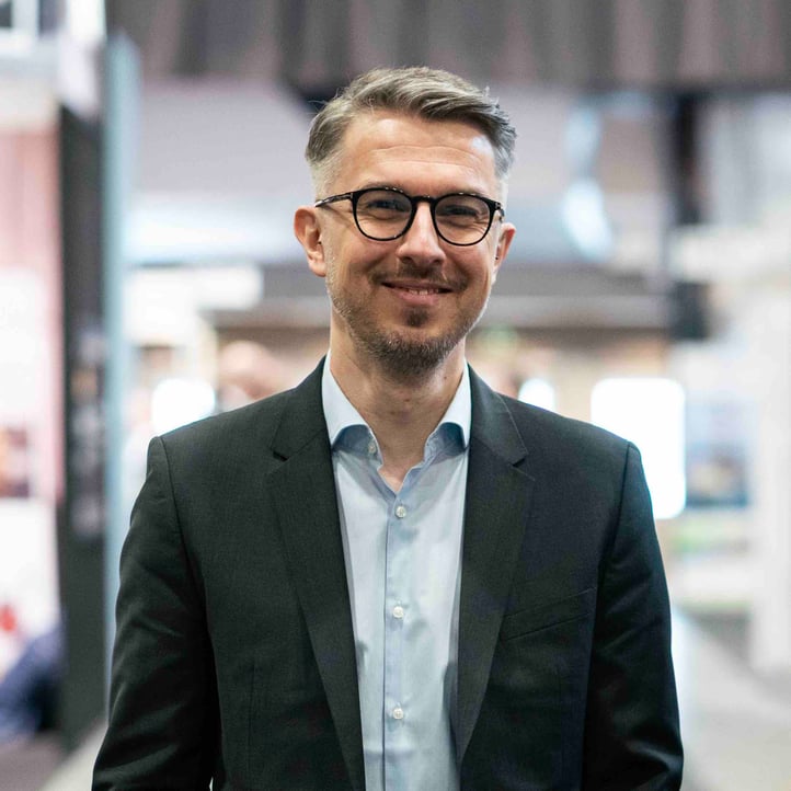 The photo shows Mr. Jakub Kwiatowski, head of R&D at Hatteland Technology. He is facing the camera, smiling. He is wearing a suit. Background blurry.