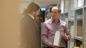 Jens Widlund og Markus Mattson from Hatteland Technology Sweden discuss logistics at the warehouse at their Stockholm office. Behind them are shelves containing technology products.