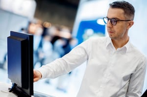 A male in a white shirt interacting with the touchscreen of an industrial Panel PC. We see the back of the Panel PC, at an angle. 