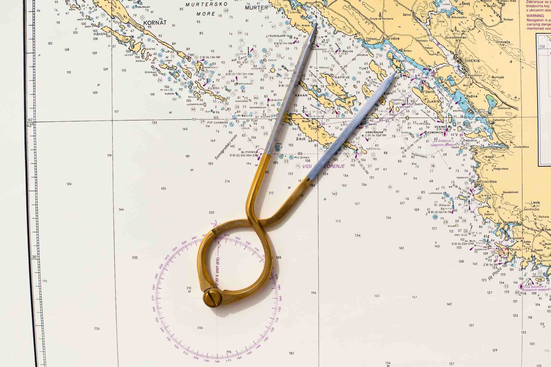 A nautical chart with a brass divider resting on top of it. The chart is in colors. 