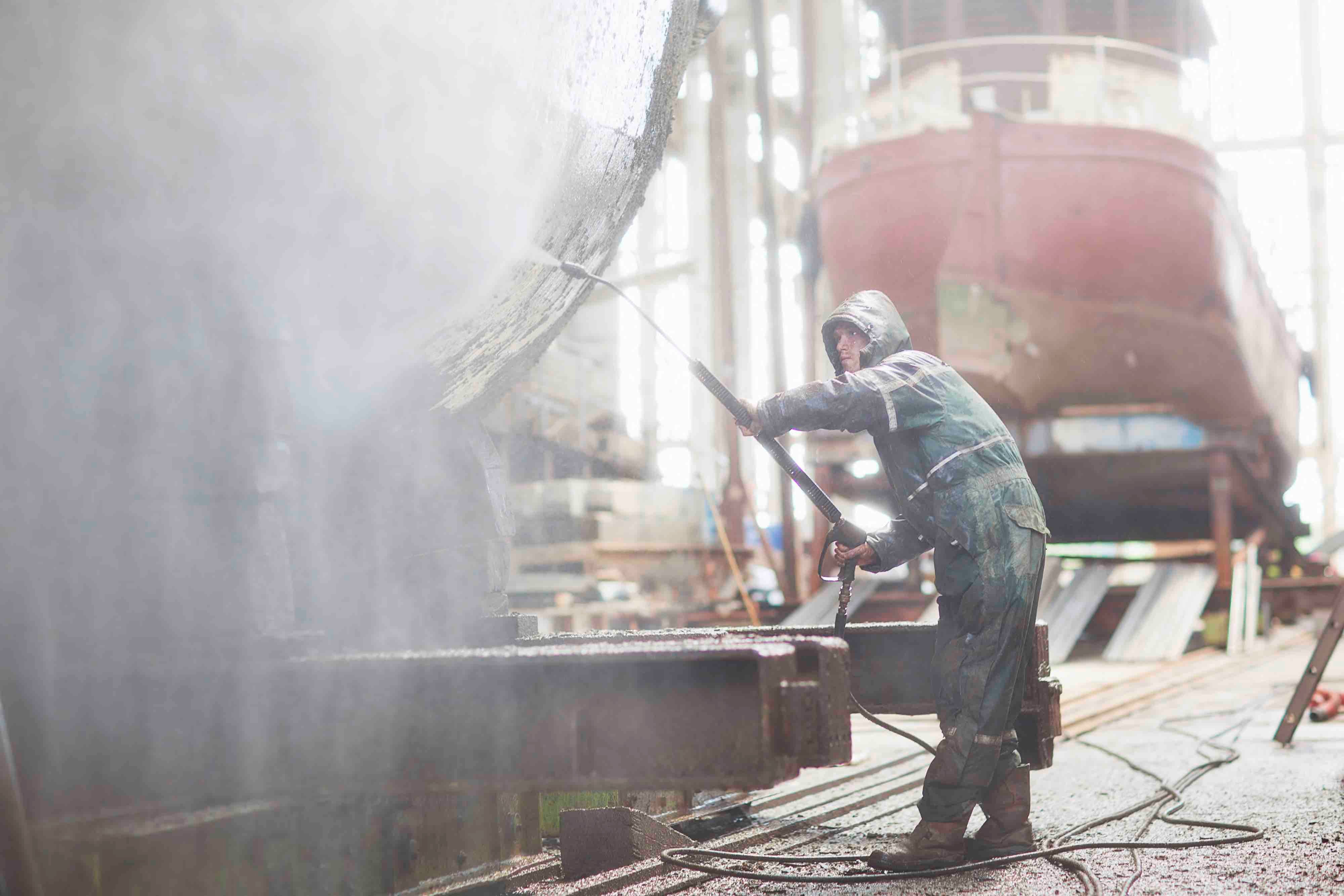 A worker is pressure washing a boat in a shipyard, with the water spray visible in the foreground. This is the sort of environment industrial computers have to be able to handle. 