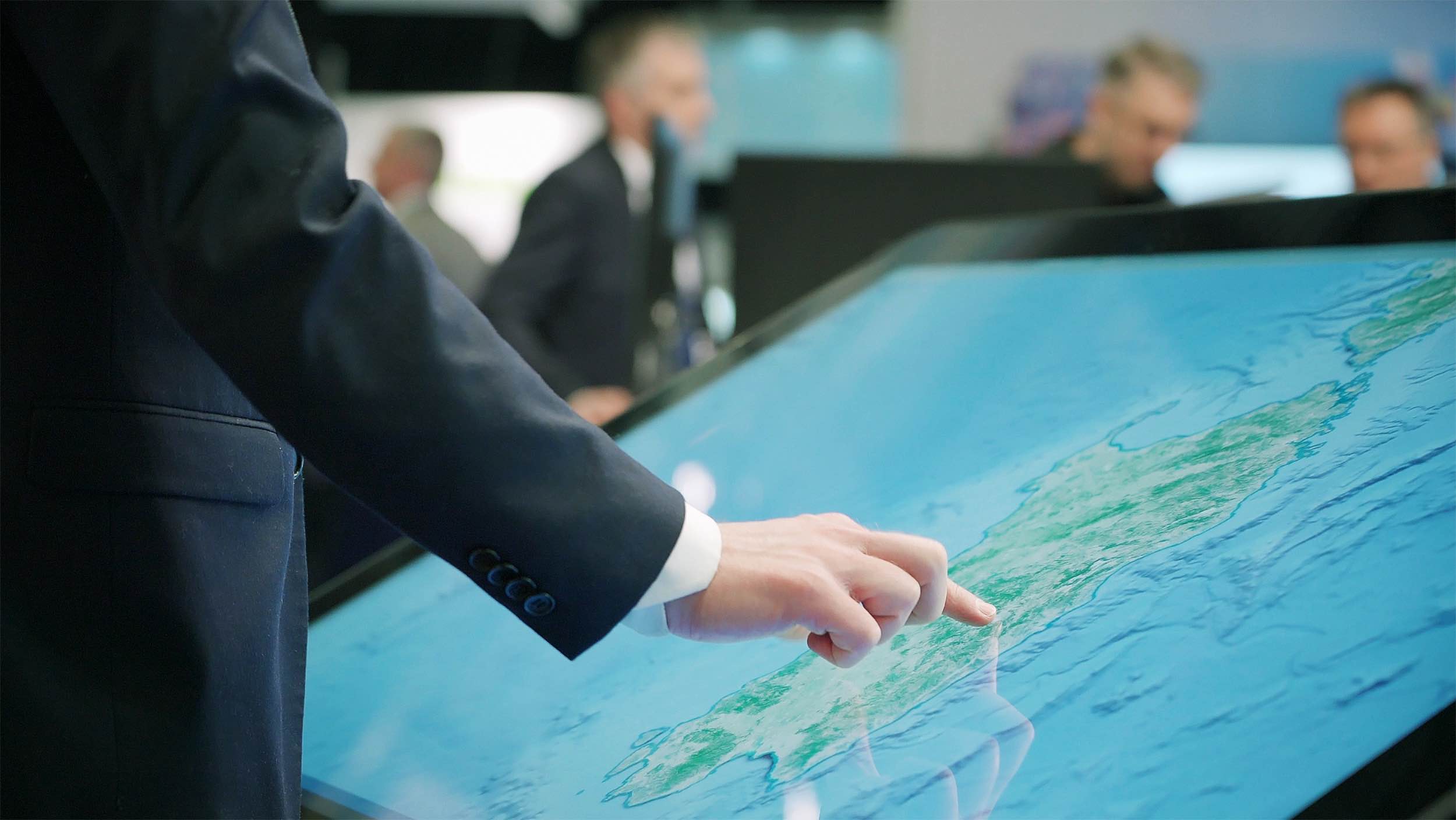 Hand interacting with Hatteland Technology's 55-inch electronic chart table, in chart or map mode.