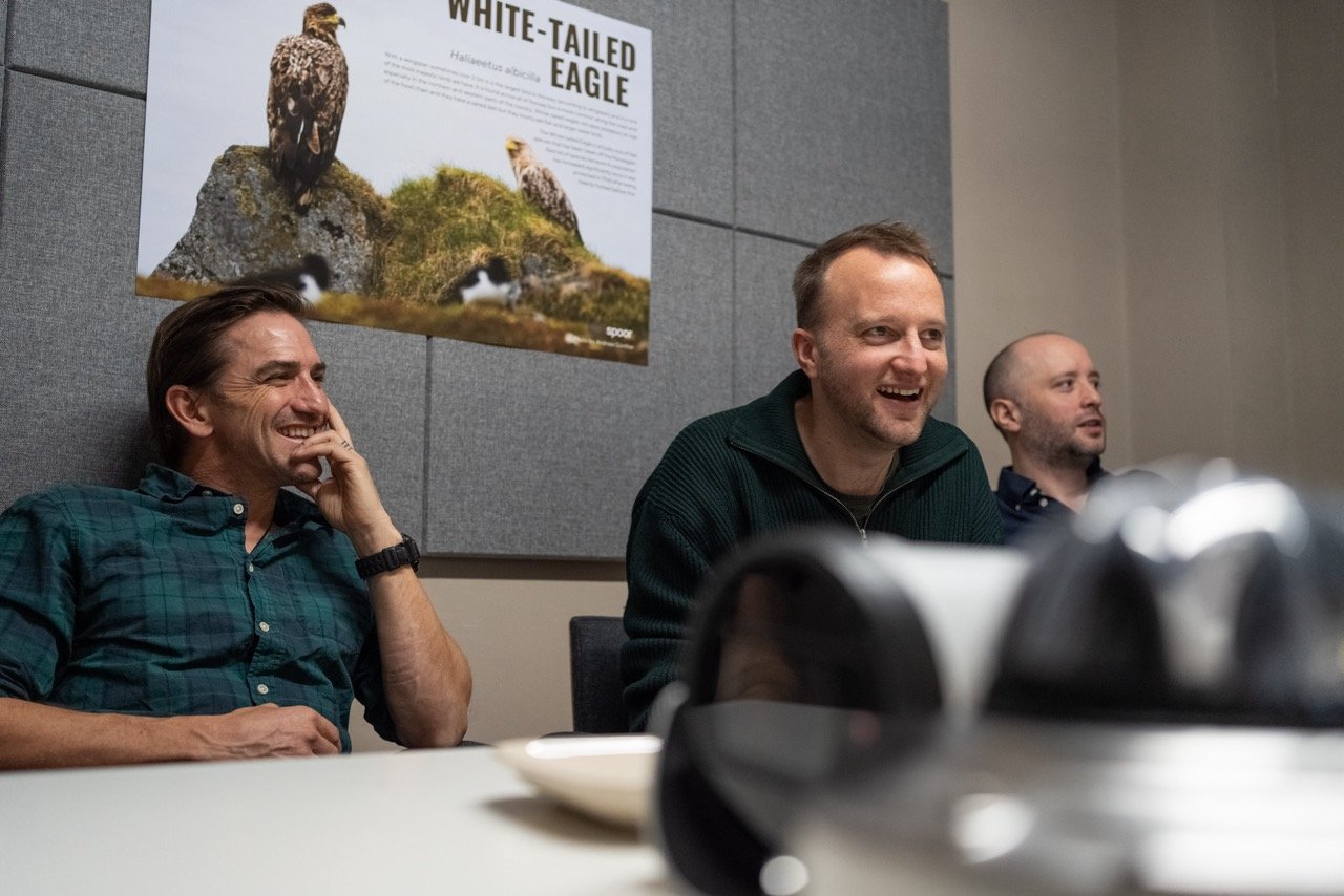 The picture shows three members of the Spoor team: Scott Behrnes, Ask Helseth, and Andrew Watts, in an office. In the background you can see a poster of two white-tailed eagles. 