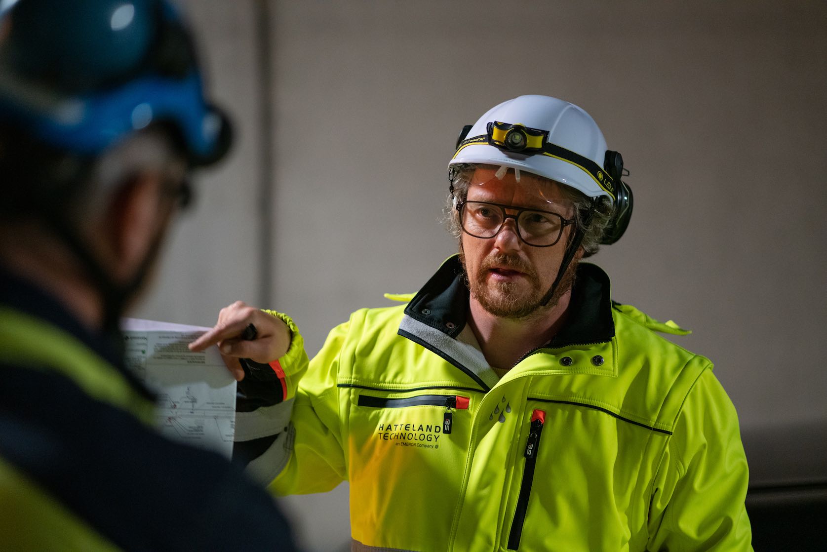 Jan Olav Larssen from Hatteland Technology is surveying a road tunnel for a surveillance solution. He's in the center of the photo, wearing a yellow, reflective suit, and a white helmet. He is conferring with a contractor. 