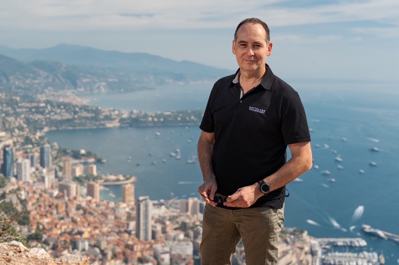 The picture shows Mr. Mehdi Bounoua, Hatteland Technology's sales director EMEA, on a hill with the bay of Monaco in the background. The bay is packed full of yachts due to the Monaco Yacht Show. The weather is nice. Mehdi is wearing a black Hatteland Technology t-shirt. 