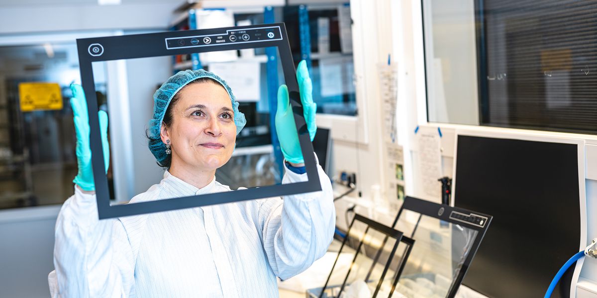 A worker is inspecting a Hatteland Technology screen for impurities under bright light. An important part of the optical bonding process. She is wearing protective gear to keep the material clean. 