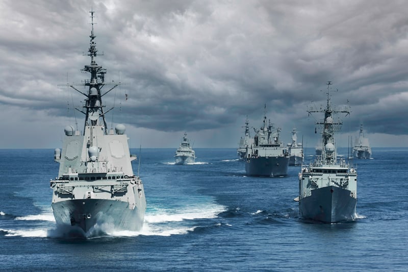 A formation of naval ships are facing the camera. The seas are calm. Above them a cloudy sky. The picture illustrates that naval & defense is one of Hatteland Technology's markets. 
